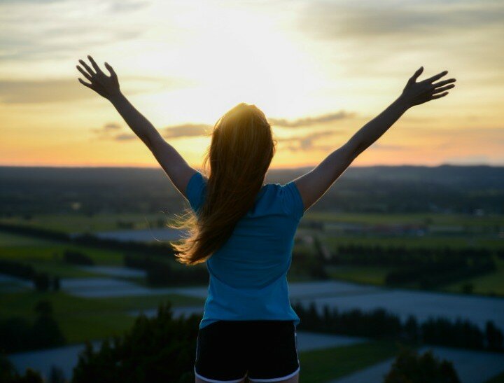 happy young woman outdoor from behind, rising her hands and looking at landscape on sunset